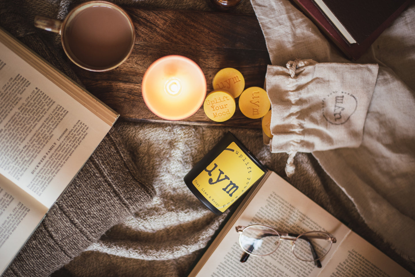 Thai Lime and Mango natural wax candle,matt black candle, matt white glass jar candle lighted, natural wax melts yellow in a cotton bag, books and a nice cup of tea, cosy atmosphere, Uplift Your Mood Scents