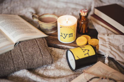 Thai Lime and Mango natural wax candle,matt black candle, matt white glass jar candle lighted, natural wax melts yellow in a cotton bag, books and a nice cup of tea, cosy atmosphere, Uplift Your Mood Scents